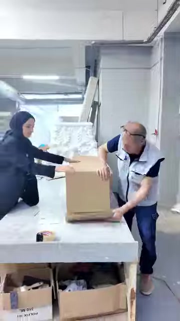Çalışanlar, beyaz dekoratif parçaları üretim masasında kutuya yerleştiriyor.