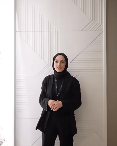 Sunucu, geometrik kabartmalarla düzenlenmiş dekoratif duvar önünde duruyor