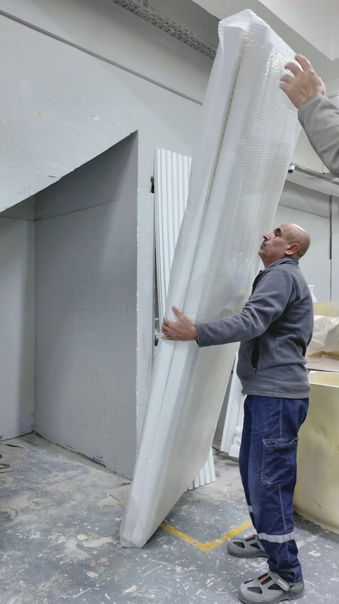 Büyük dekoratif panel iki çalışan tarafından dikkatle taşınıyor.