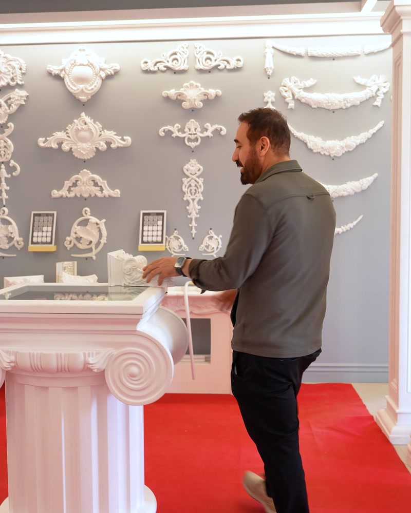 Showroom içinde beyaz sütun kaidesi yanında duran erkek