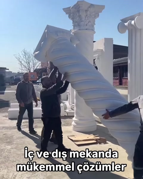 Çalışanlar büyük burgulu dekoratif sütunu birlikte taşıyor